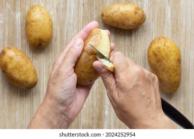 Top View Of Woman Hands Scrubbing Boiled Potato In Jacket Using Knife On Wooden Background