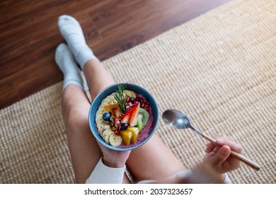 Top View Of A Woman Holding And Eating Healthy Blueberry Smoothie Bowl With Mixed Fruits Topping