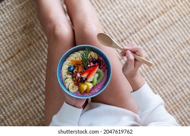 Top View Of A Woman Holding And Eating Healthy Blueberry Smoothie Bowl With Mixed Fruits Topping