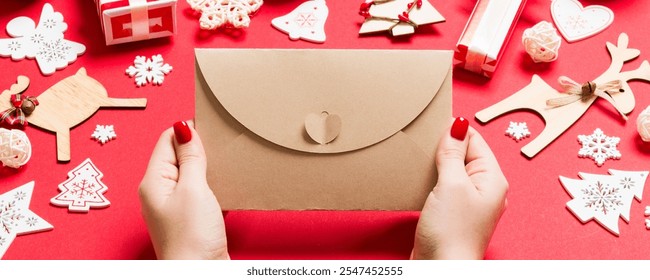 Top view of woman holding an envelope on red background made of holiday decorations. Christmas time concept. - Powered by Shutterstock