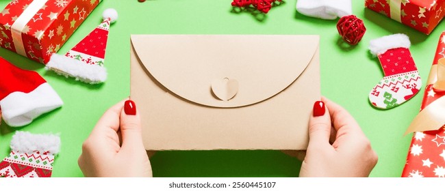 Top view of woman holding an envelope on green background made of holiday decorations. Christmas time concept. - Powered by Shutterstock