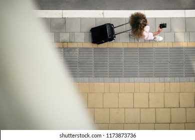 Top view of woman holding smart phone and luggage while going to the station/airport. - Powered by Shutterstock