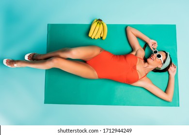 Top View Of Woman Lying Near Bananas On Beach Blanket On Blue