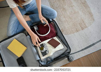 Top view of a woman preparing her belongings and packing her suitcase in the living room, getting ready for her summer vacation trip. - Powered by Shutterstock