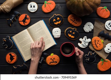 Top View Of Woman Reading Book Surrounded By Halloween Cookies