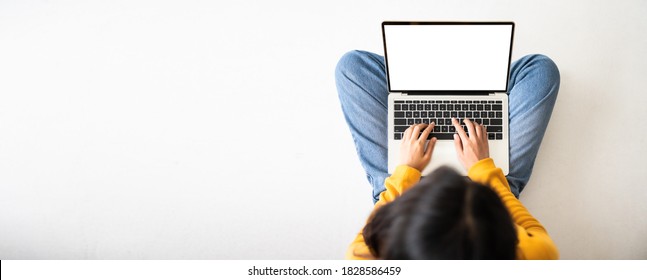 Draufsicht auf Frau, die auf dem Boden sitzt und einen weißen Bildschirm mit Laptop verwendet. Mock up, Template für den Text, Clipping Pfade für den Gerätebildschirm. Panoramabild mit leerem Kopienraum