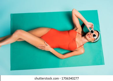 Top View Of Woman Smiling And Lying On Beach Blanket On Blue Background