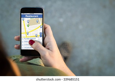 Top View Of Woman Walking In The Street Using Her Mobile Phone With Restaurant Finder On Screen With Copyspace. All Screen Graphics Are Made Up.