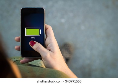 Top view of woman walking in the street using her mobile phone with full battery on screen with copyspace. All screen graphics are made up.