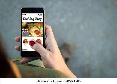 Top view of woman walking in the street using her mobile phone with cooking blog on screen. All screen graphics are made up.