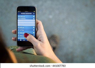 Top View Of Woman Walking In The Street Using Her Mobile Phone With Mobile Banking App. All Screen Graphics Are Made Up.