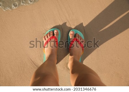 Top view of woman wearing flip flops on sandy beach, closeup