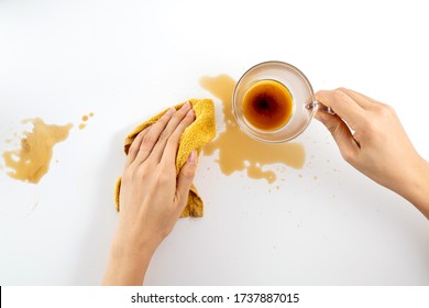 Top View Woman's Hand Cleaning Tea Stain Or Spilled Coffee On A White Table With A Yellow Dishcloth Closeup