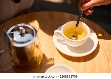 Top view of a woman's hand using a tea spoon, stirring sugar in the white teacup with healthy antioxidant herbal hot drin. Detox therapy. Tea time. Selective focus