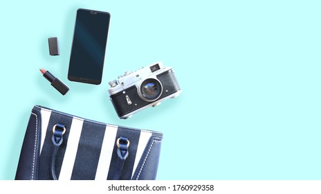                              Top view of a   woman's purse with  a cell phone, vintage camera, lipstick on isolated on light blue background  with copy space. Flatlay on blue  库存照片