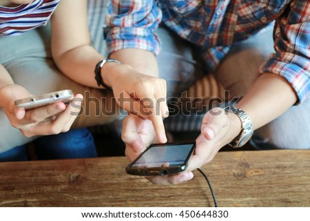 top view women working laptop and man hand use phone on wood table,the internet of things.Two young business people touching on mobile phones while working and discussion and brainstorming  in office.