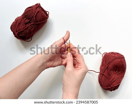 The top view of women's hands cast on loops from red woolen threads for knitting with red yarn skeins on the white background.