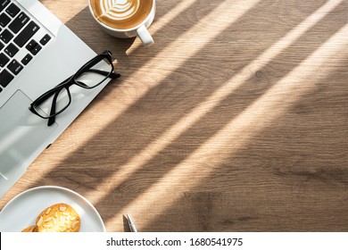 Top View Of Wood Office Desk Table With Cup Of Latte Coffee, Dish Of Almond Cookies And Office Supplies With Sun Light. Life At Work In The Morning Concept.