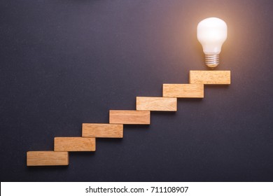 Top view wooden block set up for staircase with light bulbs on the top point on black stone board. Business success and create idea concept