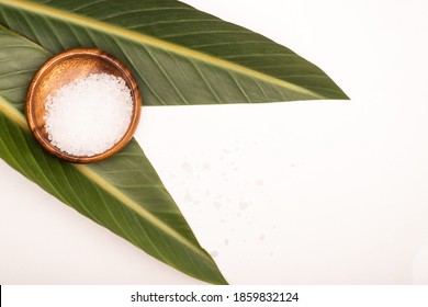 top view of wooden bowl with sea salt and green leaves on white surface - Powered by Shutterstock