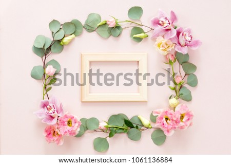Top view of wooden photo frame with copyspace and flower frame on pink background, flat lay. invitation or greeting card concept.