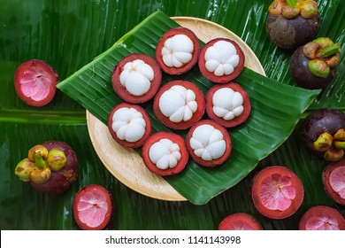 Top view wooden plate of organic cut mangosteen fruits on green banana leaf with mangosteen fruits and  purple peel background