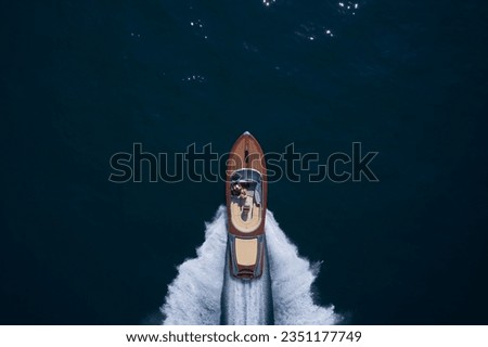 Top view of a wooden powerful motor boat. Luxurious wooden boat fast movement on dark water.Man and woman in luxury expensive wooden speedboat fast moving on dark water top view.