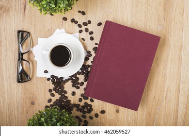 Top view of wooden surface with coffee cup on napkins, beans, glasses, decorative plants and closed hardcover book with copy space - Powered by Shutterstock