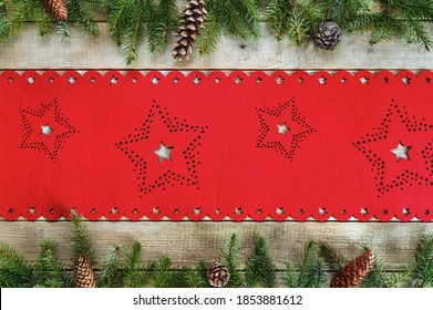 A Top View Of A Wooden Surface With A Red Christmas Table Cloth, Fir Leaves, And Cones On It