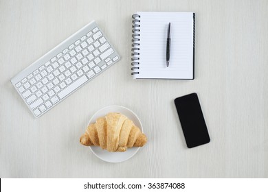 Top view of wooden table with office supplies. Office desk table with keyboard,notebook,croissant and cell phone. - Powered by Shutterstock