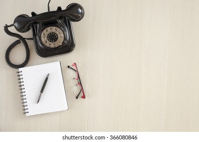 Top View Of Wooden Table With Office Supplies. Office Desk Table With Notebook,pen,glasses And Old Phone