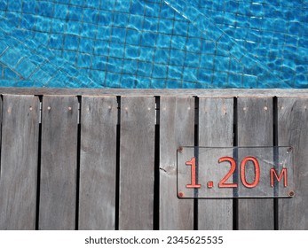 Top view wooden walkway around swimming pool, boardwalk or decking with an information sign showing numeric depth of the pool - Powered by Shutterstock