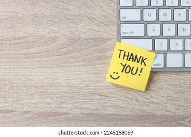 Top view of words thank you written on sticky note on keyboard over wooden background. 