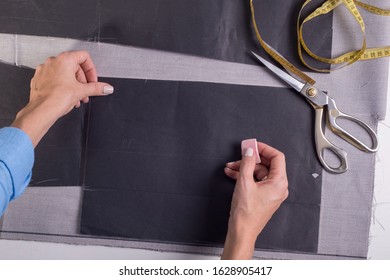 top view of the work of the hands of a master in the manufacture and sewing of clothes. Girl couturier designer with a pencil and a ruler marks the boundaries of the cut of fabric for tailoring suits