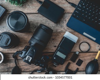 top view of work space photographer with digital camera, flash, cleaning kit, memory card, external harddisk, USB card reader and camera accessory on wooden table background.