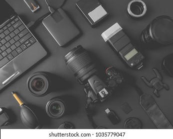top view of work space photographer with digital camera, flash, cleaning kit, memory card, external harddisk, USB card reader, laptop and camera accessory on black table background