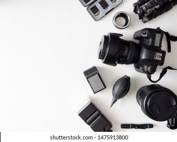 Top View Of Work Space Photographer With Digital Camera, Flash, Cleaning Kit, Memory Card, Tripod And Camera Accessory On White Table Background