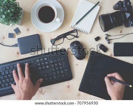 top view work space of photographer hand  or creative designer hand with digital camera, computer keyboard, memory card, graphic tablet, coffee cup, mouse on wooden table.