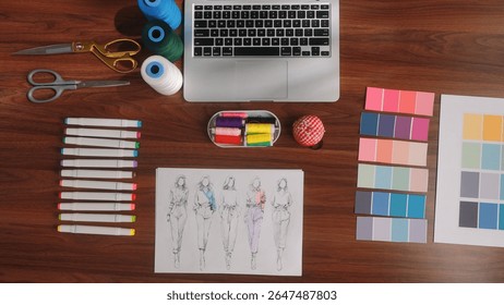 Top view of the Work Zone, where the main tools for fashion design are presented colored threads, markers and sketches, fabric samples and a laptop for working with digital technologies.