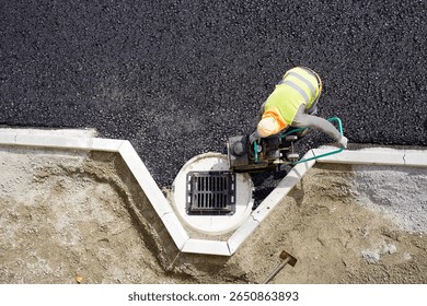 Top view of worker using vibrSation plate to compact fresh asphalt around water drainage cover