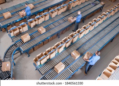 Top View Of Workers Packing Boxes On Conveyor Belts At A Distribution Warehouse.