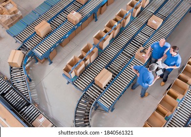 Top view of workers with papers and a digital tablet having a discussion among boxes laid on conveyor belts at a distribution warehouse. - Powered by Shutterstock