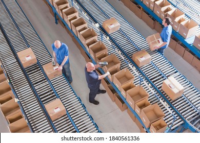 Top View Of Workers Scanning Boxes On Conveyor Belts At A Distribution Warehouse.