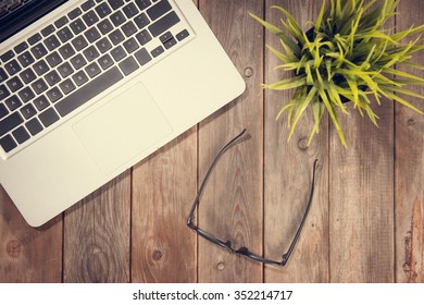 Top View Working Desk With Laptop Computer, Eyeglasses And Plant Pot. Instant Photo Vintage Split Toning Color Effect.