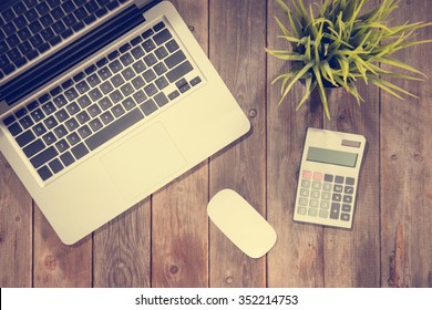 Top View Working Desk With Laptop Computer, Calculator And Plant Pot. Wooden Table Background With Copy Space In Vintage Toned.