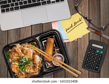 Top View Of Working Space With Word  Lunch Break On Paper Note, A Box Of Shrimp Fried Rice And Spring Roll, Computer Laptop, Pen, Eye Glasses And A Calculator. 