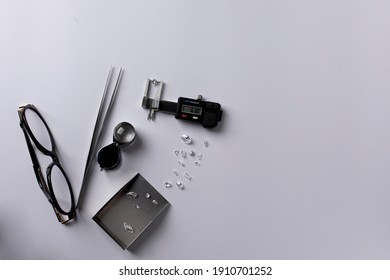 Top view of workplace of expert diamond appraiser. Heard cut diamond in measuring device. Diamonds of different sizes and shapes, tweezers, magnifier, scoop and glasses on white background