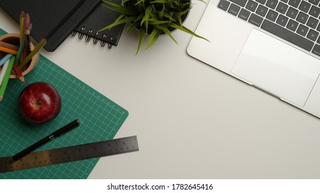 Top view of workspace with copy space, laptop, cutting mat, stationery, notebooks and plant pot on white desk - Powered by Shutterstock