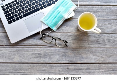 
The top view of the workspace during the covid19 (coronavirus) is spreading with a laptop computer, nose mask, glasses, and a cup of herbal drink on a gray wooden table.The idea for coping and virus  - Shutterstock ID 1684133677