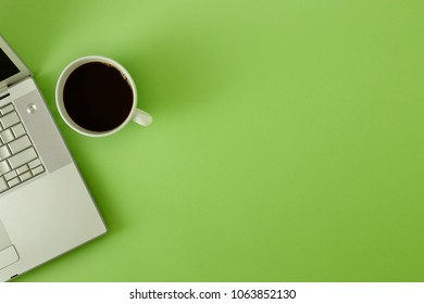 Top view of workspace with laptop, cup of coffee and copy space on green pastelbackground